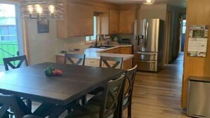 A modern kitchen with wooden cabinets, a stainless steel refrigerator, and a dining area with a dark wooden table and chairs.