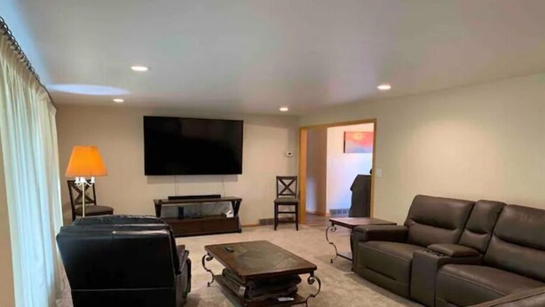 A living room with a large flat-screen TV, a brown leather sofa, a coffee table, and a lamp.
