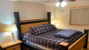 A bedroom with a bed, two bedside tables, a ceiling fan, and a window with blinds.