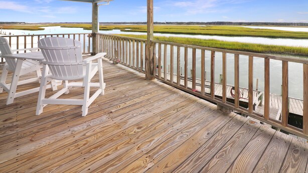 Une terrasse en bois, agrémentée de chaises Adirondack, qui offre une vue sur un paysage marécageux avec de l’eau et de la végétation.