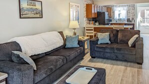 A living room with two dark grey sofas, a white throw blanket, and a white cutting board on an ottoman. - Heron Landing | Remodeled Coastal Cottage, Walk/Bike to Memorial Park (Chincoteague Island)