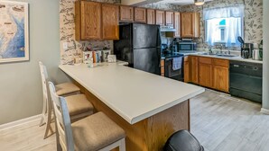 A kitchen with wooden cabinets, a black refrigerator, a microwave, and a sink. - Heron Landing | Remodeled Coastal Cottage, Walk/Bike to Memorial Park (Chincoteague Island)