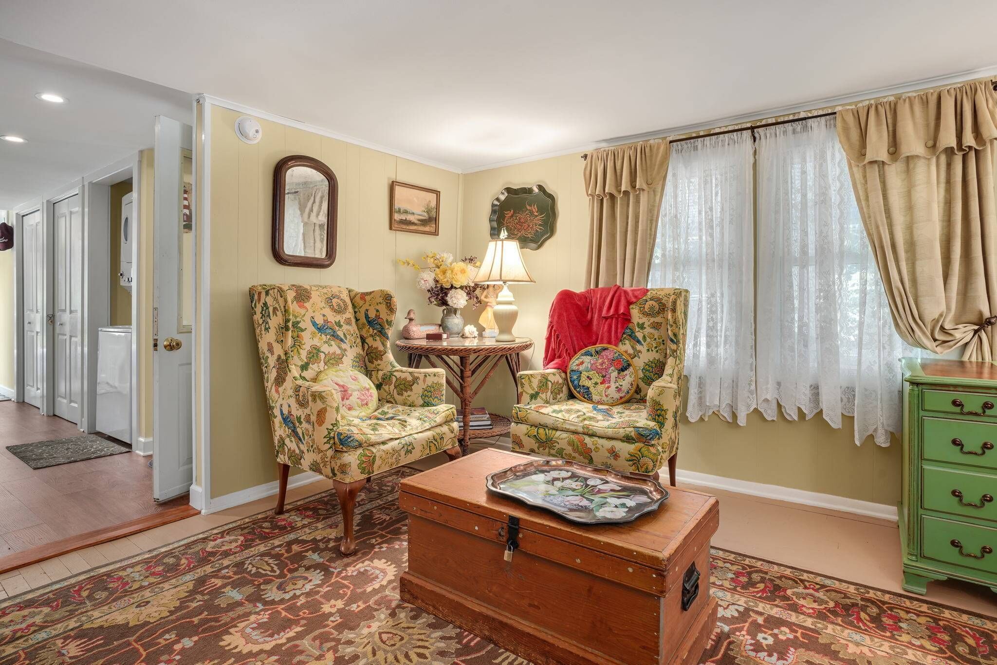 A living room with floral armchairs, a wooden chest of drawers, and a patterned rug.