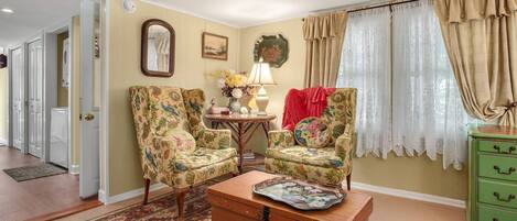 A living room with floral armchairs, a wooden chest of drawers, and a patterned rug.