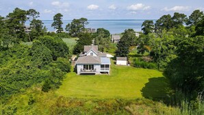 A house with a large lawn and a view of the sea. - Homestead | Historic Cottage on 30 Acres, Porches, Bay Breezes, Outdoor Shower, Nature Retreat (Chincoteague Island)