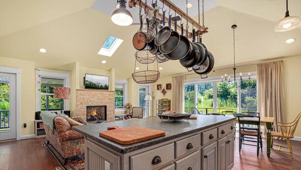 A spacious kitchen with a large island, hanging pots, and a fireplace. - Homestead | Historic Cottage on 30 Acres, Porches, Bay Breezes, Outdoor Shower, Nature Retreat (Chincoteague Island)
