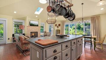 A spacious kitchen with a large island, hanging pots, and a fireplace.