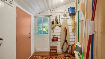 A hallway with a wooden door, a small wooden stool, a surfboard, and cleaning tools.