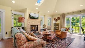 A spacious living room with a fireplace, comfortable seating, and a large window offering a view of the outdoors.