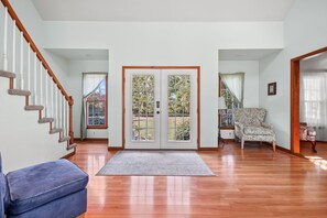 Una sala de estar amplia con una escalera de madera, un puerta doble con paneles de vidrio, un sofá azul y un sillón estampado.