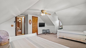 A bedroom with two beds, a ceiling fan, a TV, a small table, and a chair.