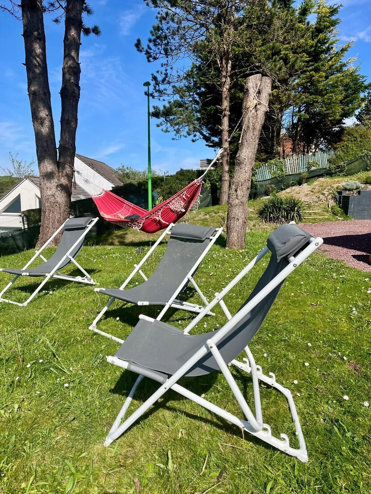 Poltrone da esterno e un'amaca in un'area erbosa con alberi e un edificio sullo sfondo.