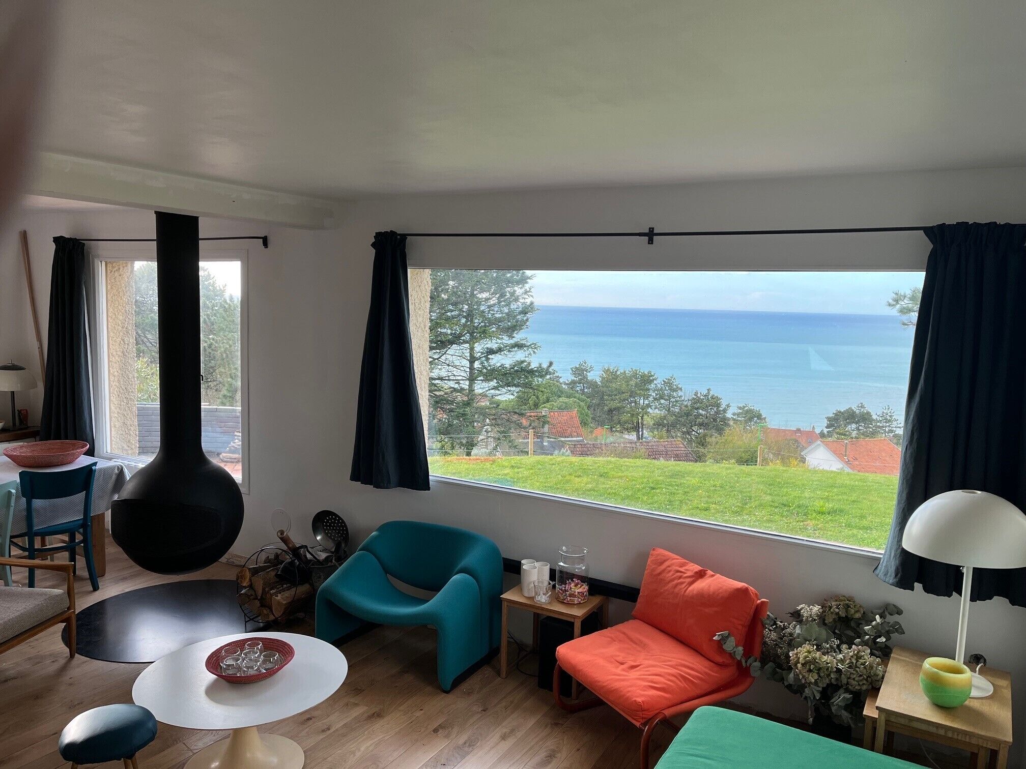 Un salon spacieux doté d’une grande fenêtre offrant une vue sur la mer et la verdure.