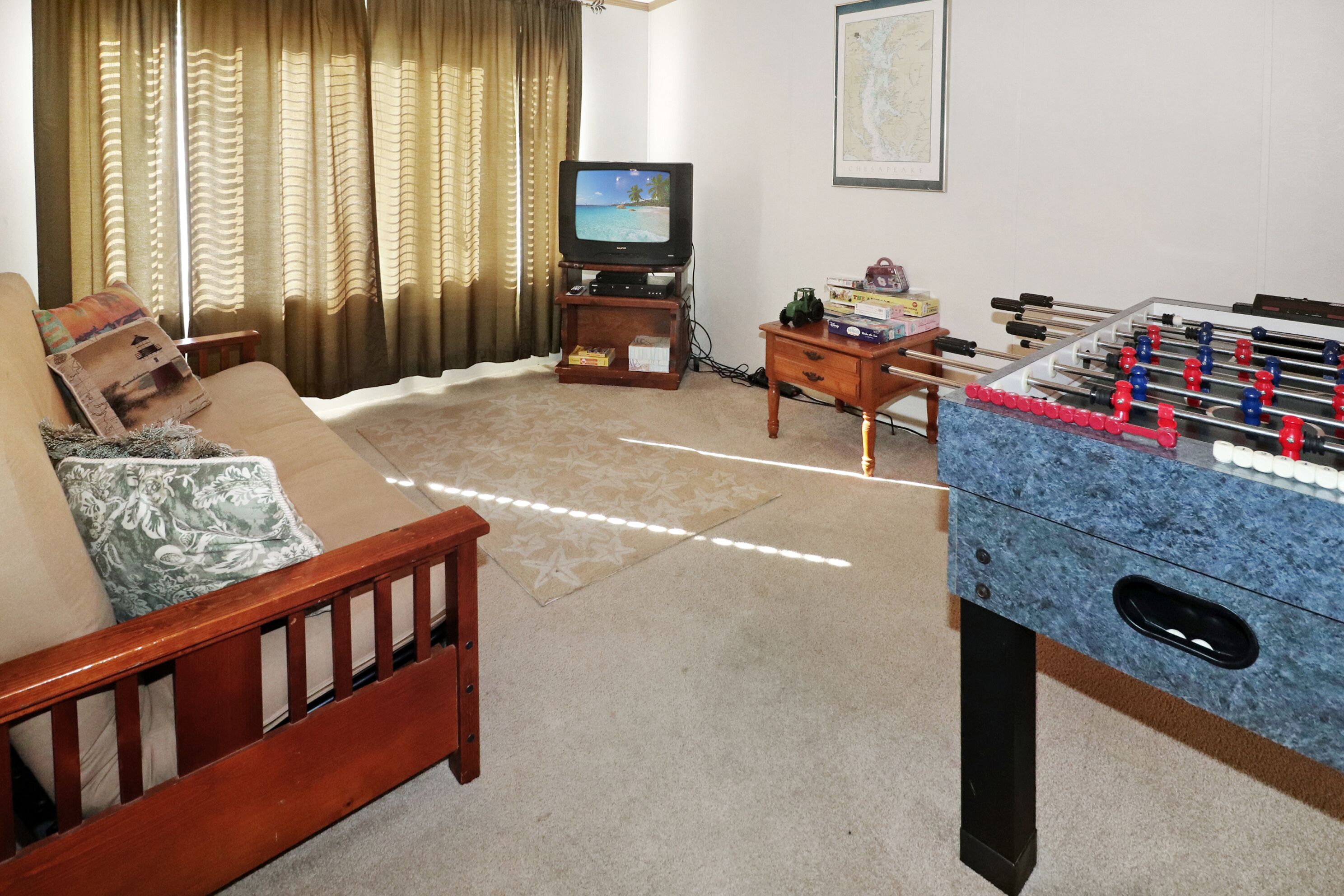 Ein Wohnzimmer mit einer Couch, einem Fernseher, einem Kicker und einem kleinen Holztisch mit Büchern und einer Dekoration.