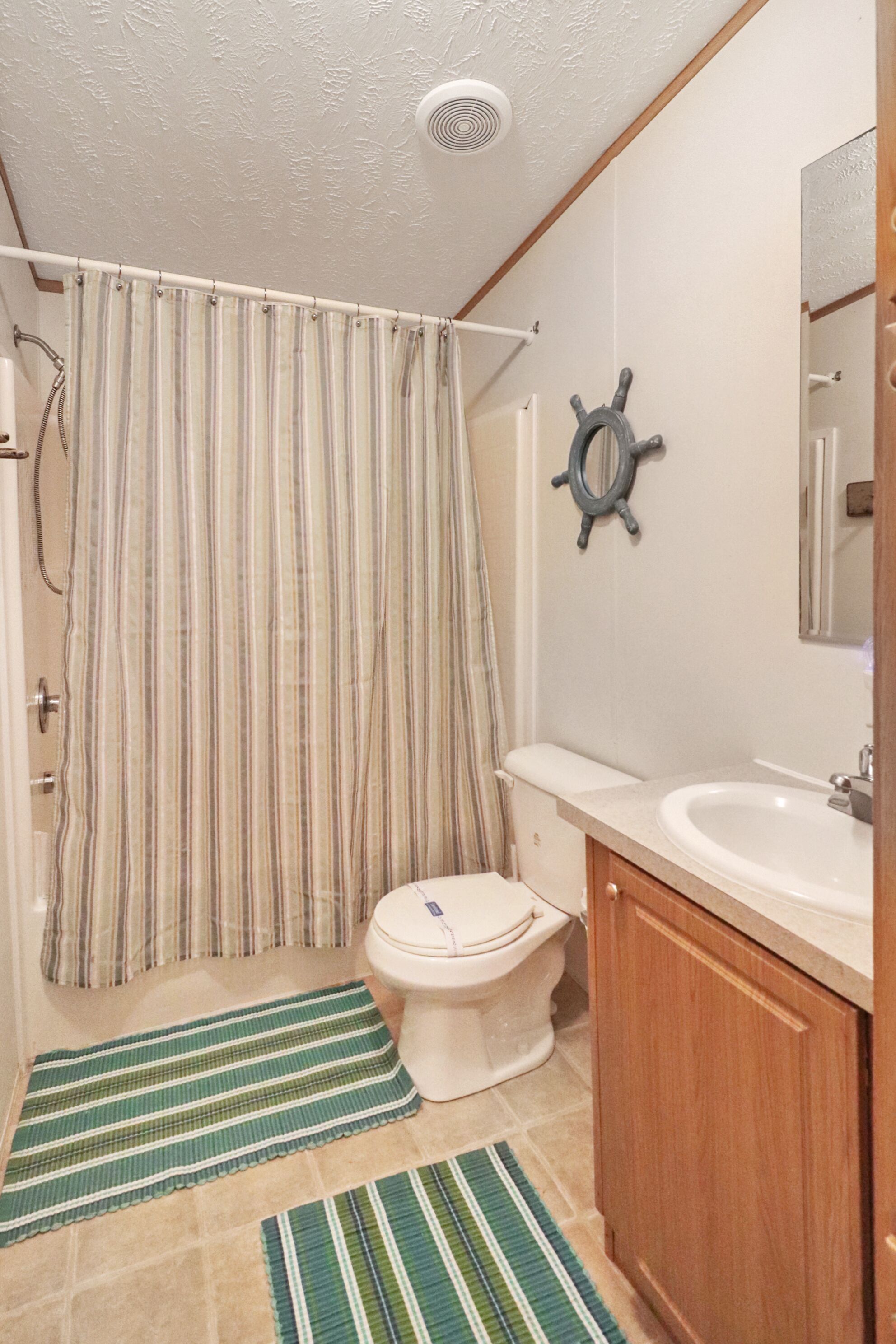Ein Badezimmer mit gestreiftem Duschvorhang, einer Schiffslenken-Dekoration, einer Toilette und einem Holzkabinet.