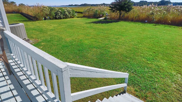 A view from a porch overlooking a well-maintained lawn with a wooden railing. - Joint Venture | Walk to Maddox Blvd, Water Views, Affordable Stay + Pet Friendly (Chincoteague Island)