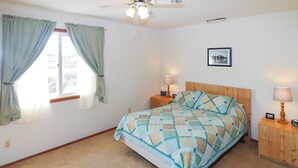A bedroom with a bed, two bedside tables, a ceiling fan, a window with curtains, and a framed picture on the wall. - Joint Venture | Walk to Maddox Blvd, Water Views, Affordable Stay + Pet Friendly (Chincoteague Island)