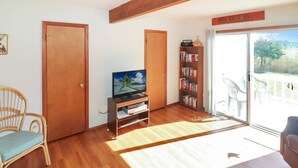 A living room with a television, bookshelf, and a sliding glass door to an outdoor area. - Joint Venture | Walk to Maddox Blvd, Water Views, Affordable Stay + Pet Friendly (Chincoteague Island)