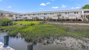 A row of white motel buildings with balconies and a grassy area in front. - Joint Venture | Walk to Maddox Blvd, Water Views, Affordable Stay + Pet Friendly (Chincoteague Island)