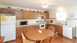 A kitchen with wooden cabinets, a refrigerator, a stove, a sink, and a dining table with chairs. - Joint Venture | Walk to Maddox Blvd, Water Views, Affordable Stay + Pet Friendly (Chincoteague Island)