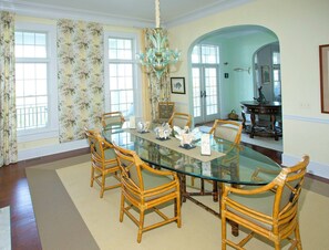 A dining room with a glass table surrounded by wicker chairs, floral wallpaper, and a chandelier.