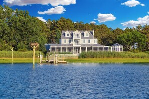 A large, two-story house with a dock extending into a lake, surrounded by lush greenery.
