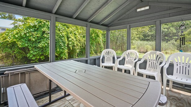 A covered outdoor area with a table and chairs, large windows, and greenery outside. - Lazy Days | Main Street Cottage w/ Snippet Bay Views, Close to Town + Trails, Pet Friendly (Chincoteague Island)