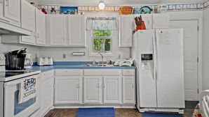 Una cucina compatta con mobili bianchi, un piano di lavoro blu, un frigorifero e una finestra vista verde.