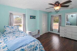 Un dormitorio con cama, cómoda, ventilador de techo y ventana con cortinas.