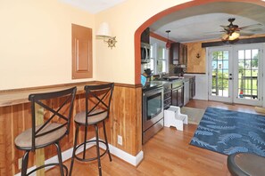 Una cocina con taburetes de madera, horno empotrado y vistas al exterior a través de una puerta de cristal.