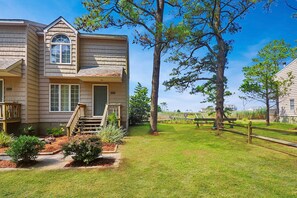 Une maison à deux étages avec un porche à l’avant, un petit jardin et une terrasse en bois.