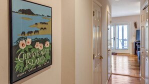 A hallway with a framed poster of Chincoteague Island, a door, and a staircase leading to another room.