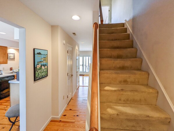 Un escalier dont les marches sont recouvertes de moquette et qui possède une rampe en bois, menant à l’étage supérieur.