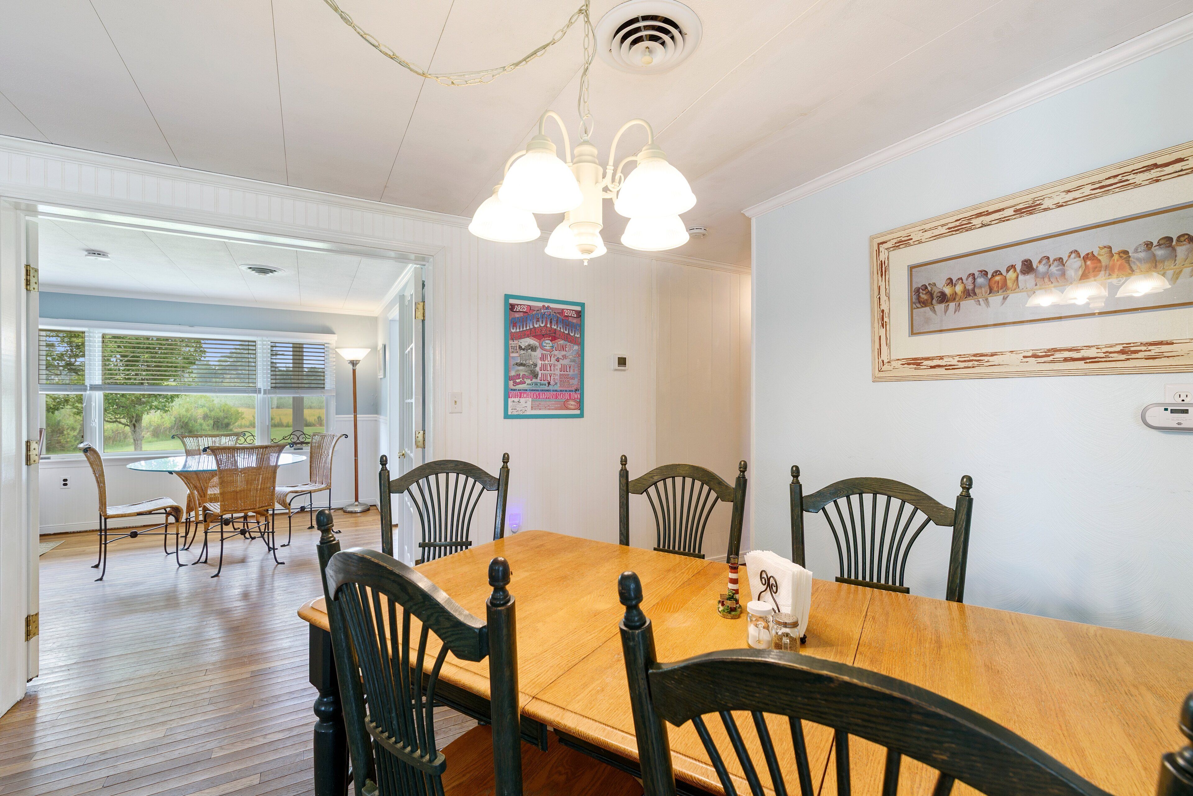 A dining room with a wooden table and chairs, a chandelier, and a framed picture on the wall.