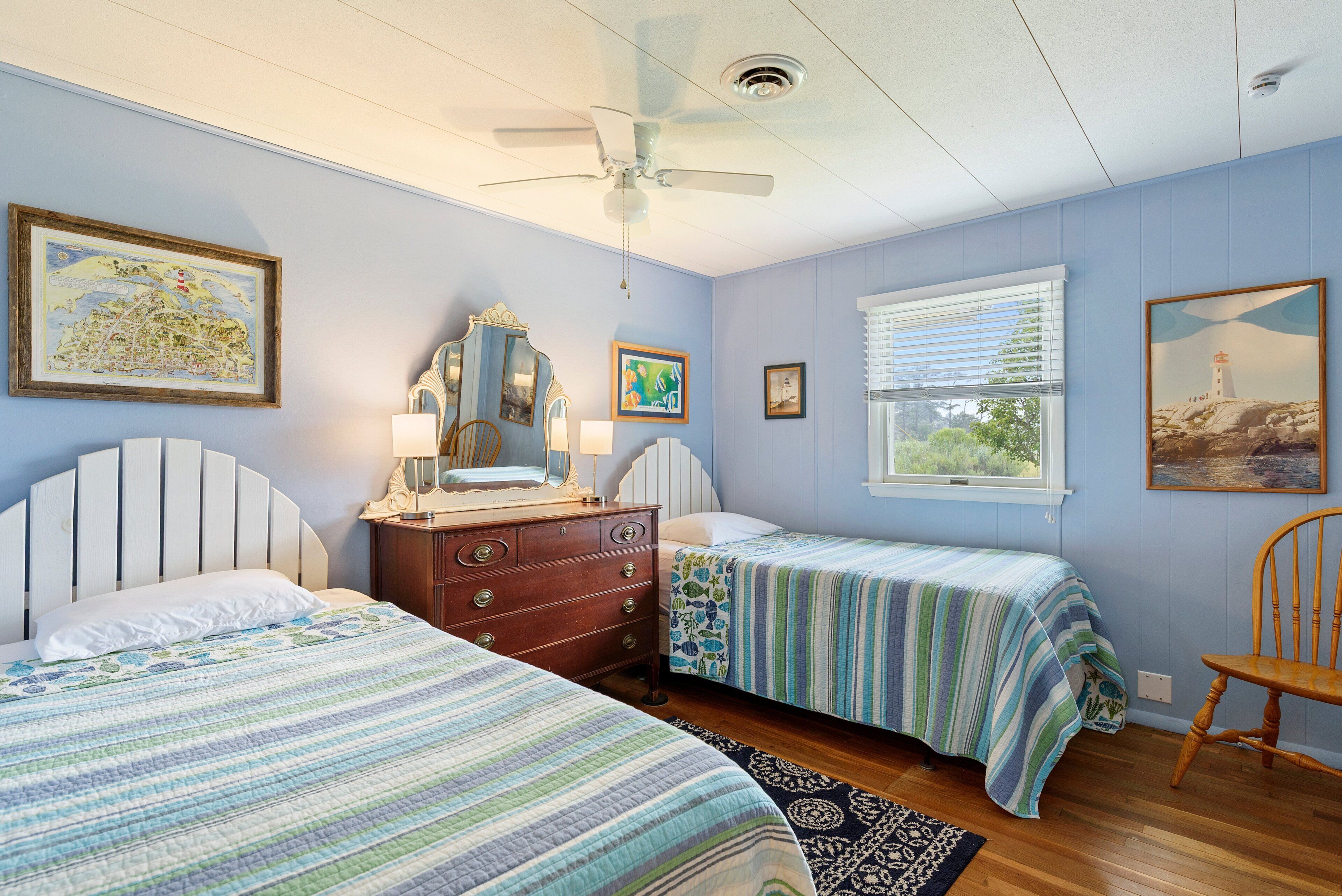A bedroom with two beds, a dresser, a ceiling fan, and artwork on the walls.
