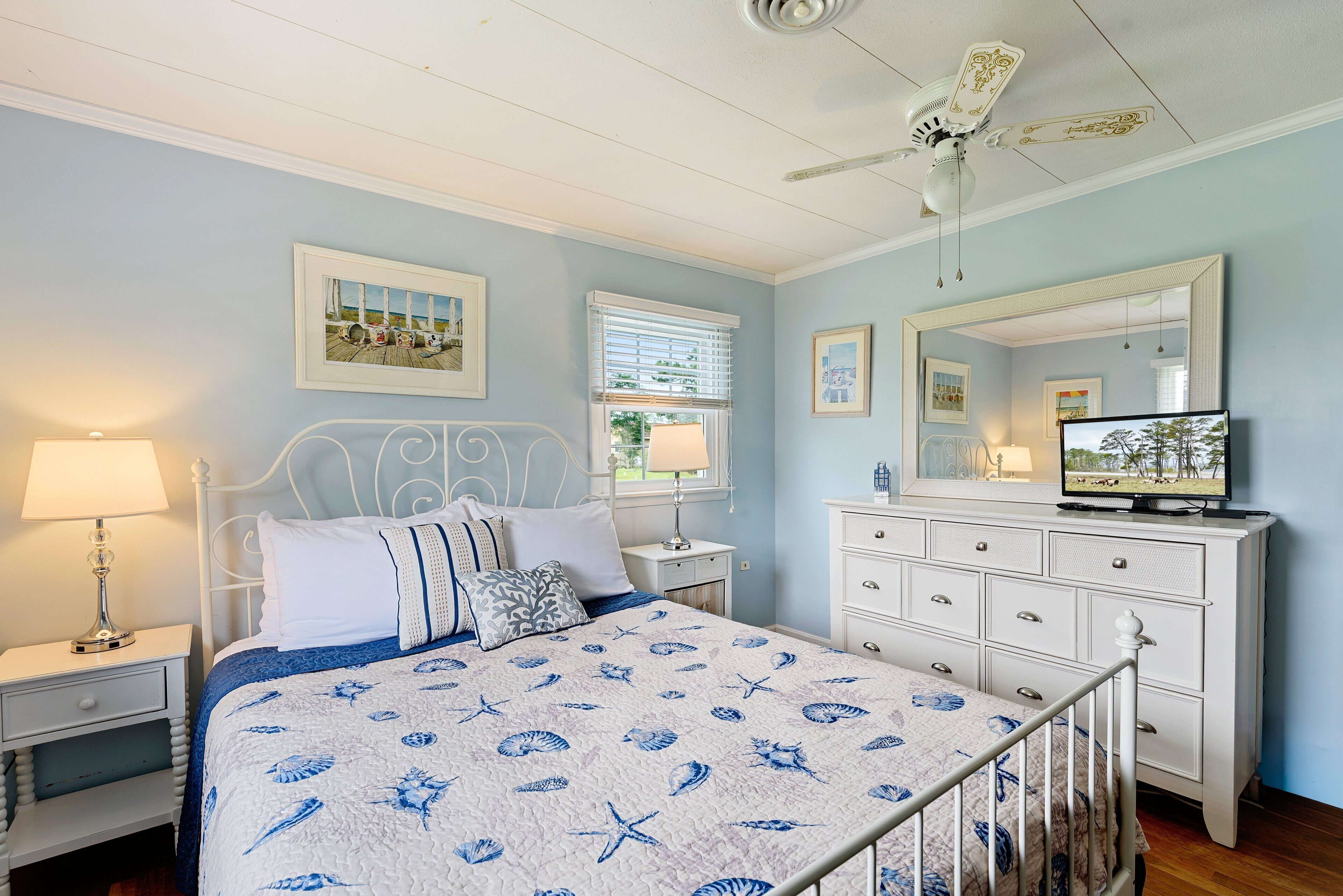A bedroom with a bed, bedside tables, a dresser, a ceiling fan, and a television.