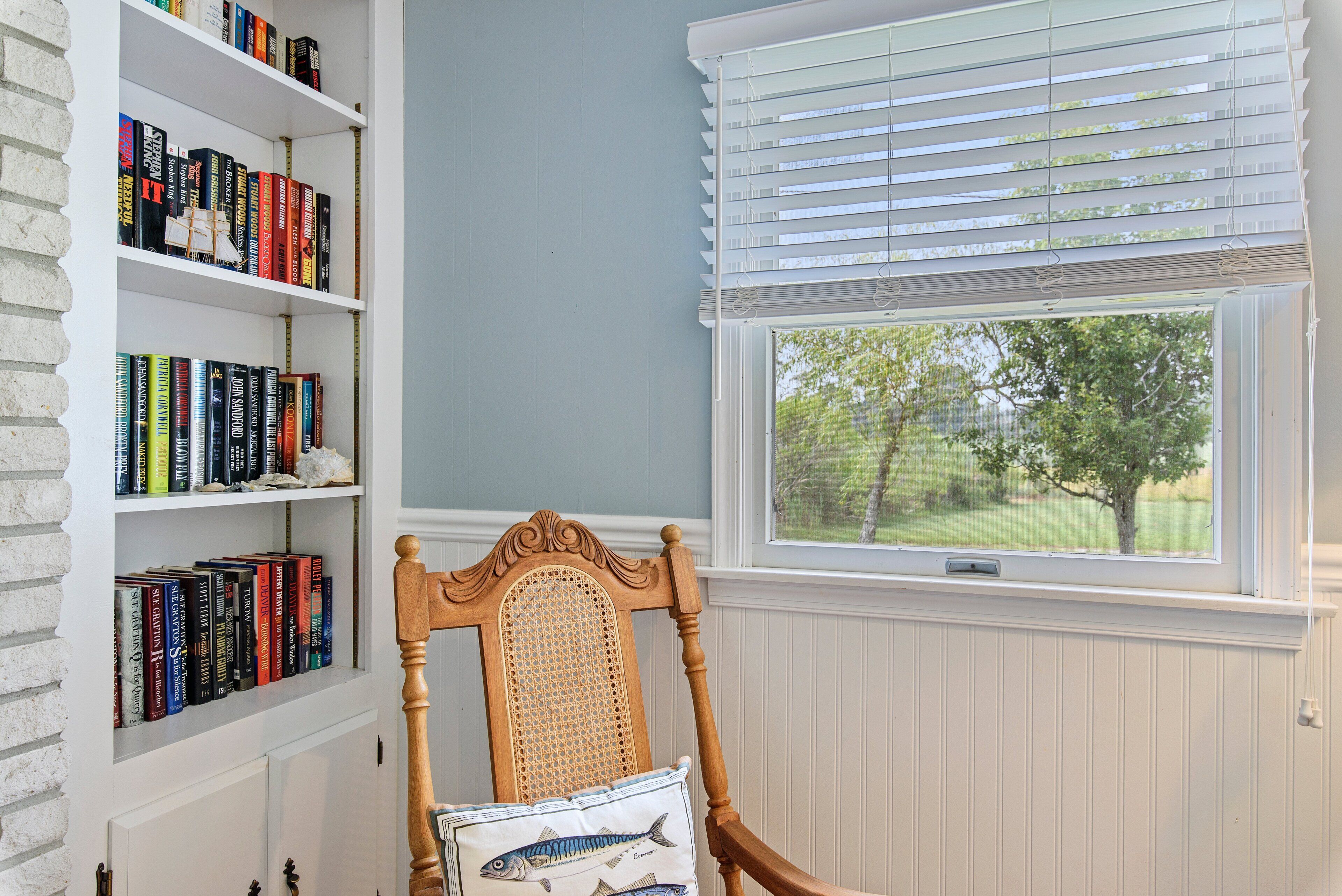 A room with a bookshelf, a chair, and a window with blinds.