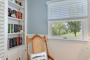 Une pièce avec une bibliothèque, une chaise et une fenêtre avec des stores.