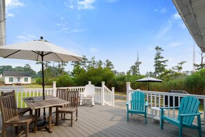 Une terrasse en bois, aménagée avec du mobilier d’extérieur, notamment une table et des chaises, et dotée d’une rambarde blanche.