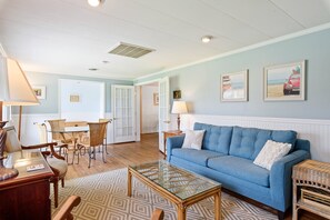 A living room with a blue sofa, a glass coffee table, wicker furniture, and a door leading to another room.