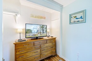 A wooden dresser with a flat-screen TV, two lamps, and a sign above the TV.