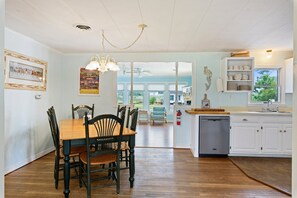Een eetgedeelte met een houten tafel en stoelen, een keuken met witte kasten, en uitzicht door de glazen deur.