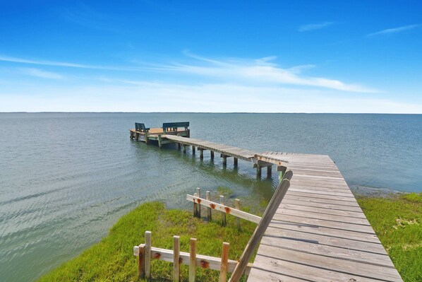 A wooden pier extending into calm water, with benches and a grassy area at the end.