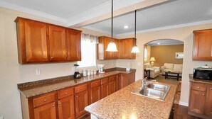 A kitchen with wooden cabinets, granite countertops, and pendant lighting. - My Island Escape | Luxury New Home, Gourmet Kitchen, Soaking Tub, Deck Retreat Near North Main (Chincoteague Island)