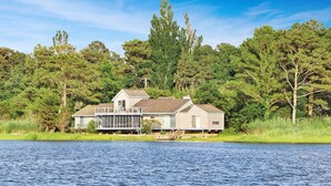 A house by a lake with a large deck and a covered outdoor area. - Poole's Cove | Waterfront Main Street Retreat Fully Renovated w/ Rooftop Lounge & Artistic Charm (Chincoteague Island)