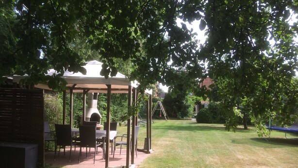 A covered patio area with a grill, seating, and a swing set in a backyard.