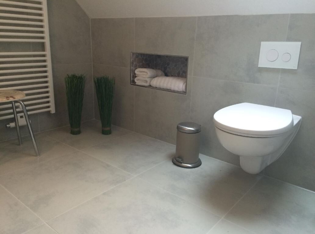 Un bagno con il water, un cestino, un portasciugamani con asciugamani e un termosifone.