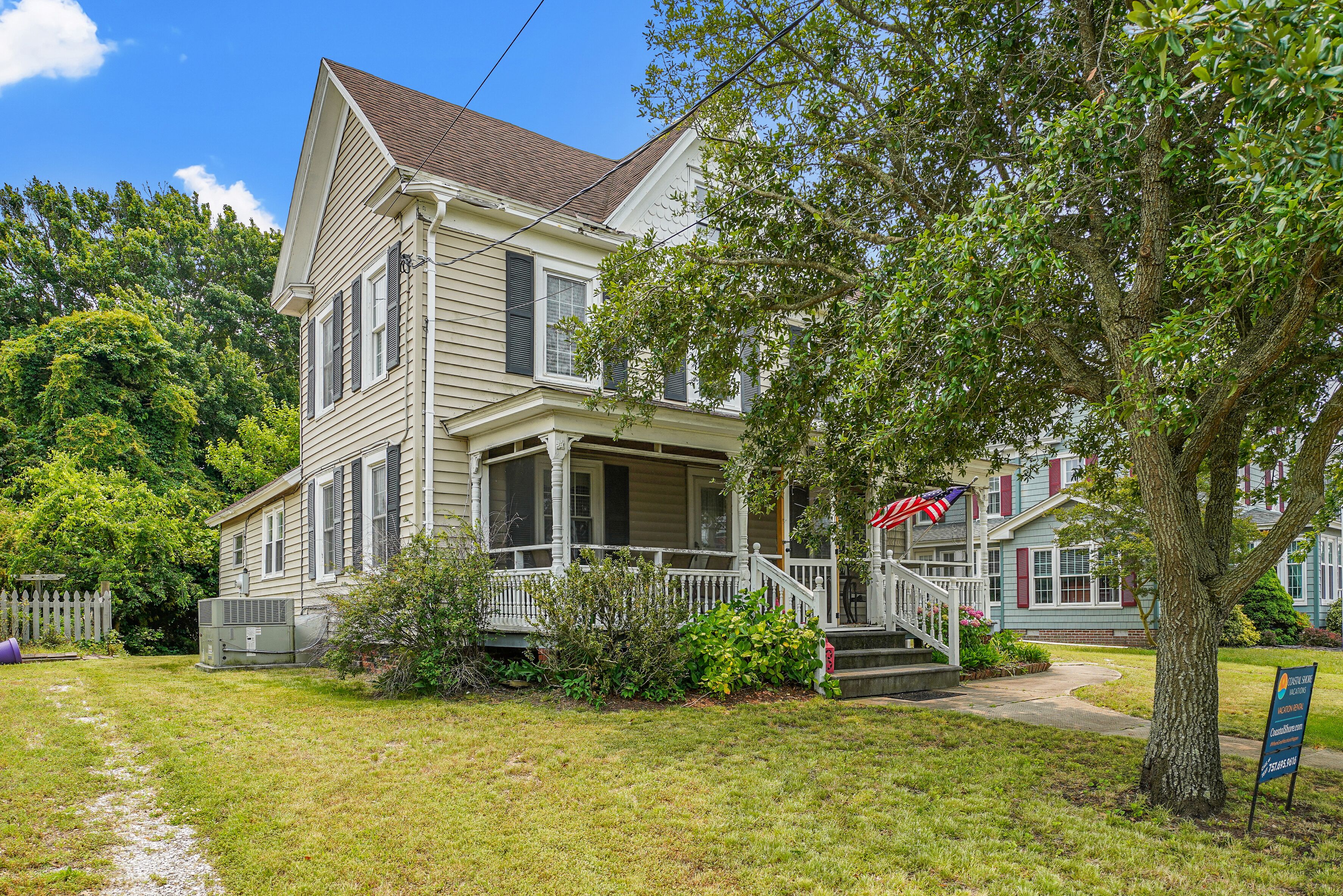 A two-story house with a porch, a flag, and a signboard.