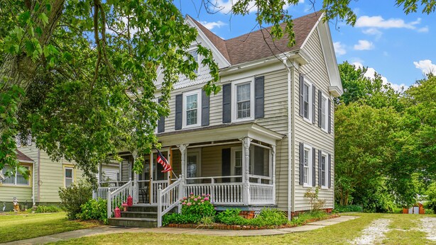 A two-story house with a porch, a front yard, and a flag. - Serendipity | Classic Chincoteague Home Walk to Main Street w/ Screened Porch & First-Floor Bedroom (Chincoteague Island)