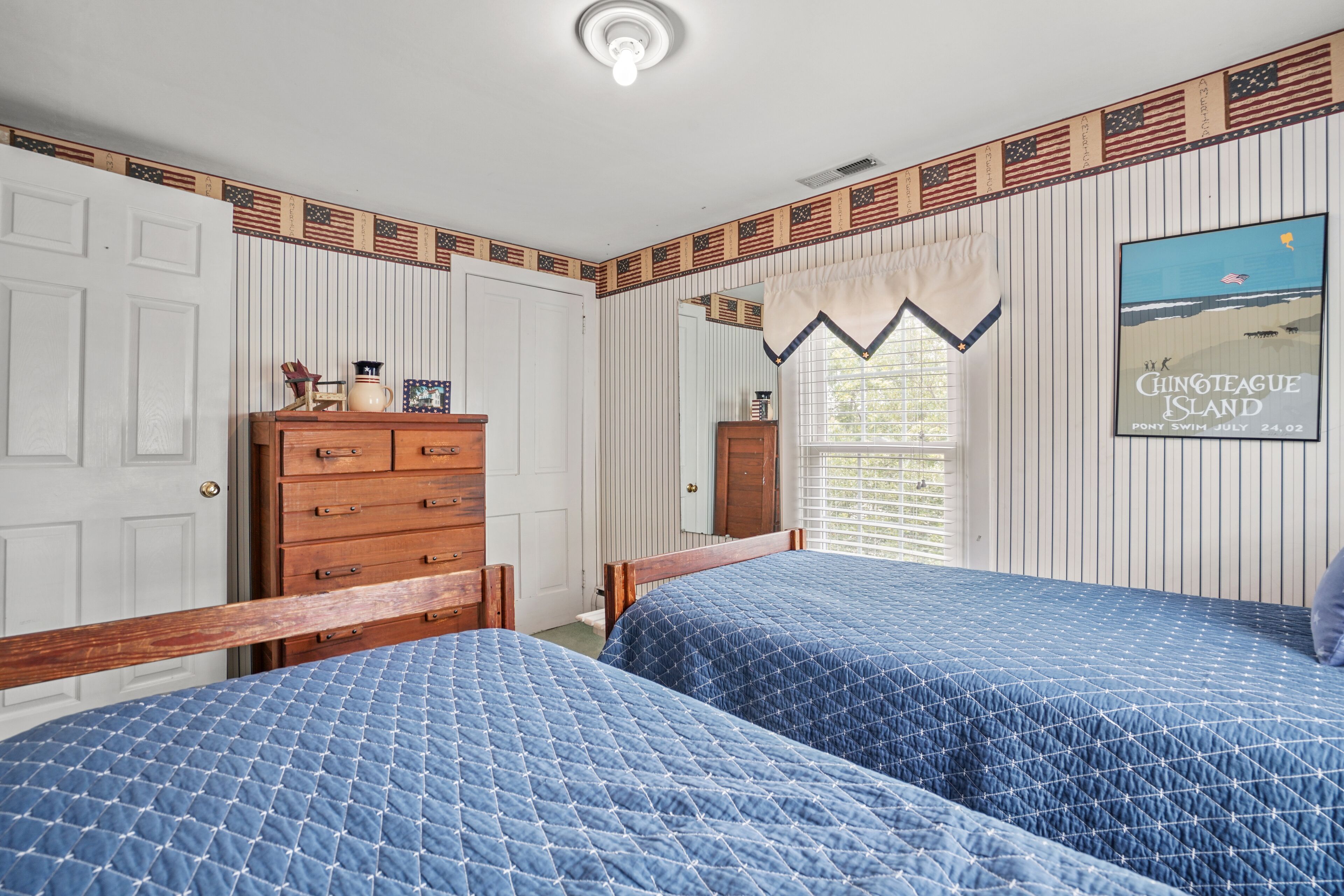 A bedroom with two beds, a dresser, and a window with blinds.